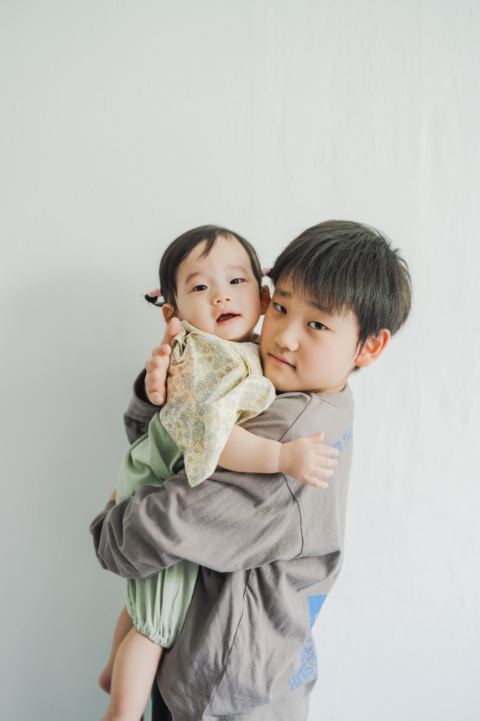 兄が赤ちゃんの妹を優しく抱っこしているスタジオ家族写真