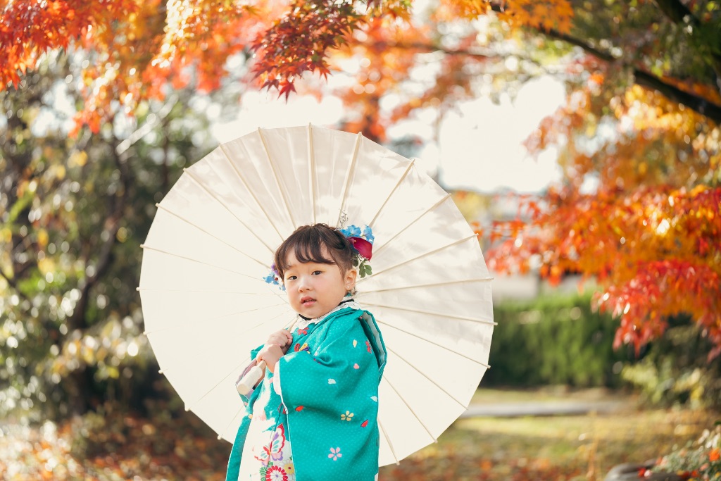 紅葉の中で番傘をさす七五三の女の子