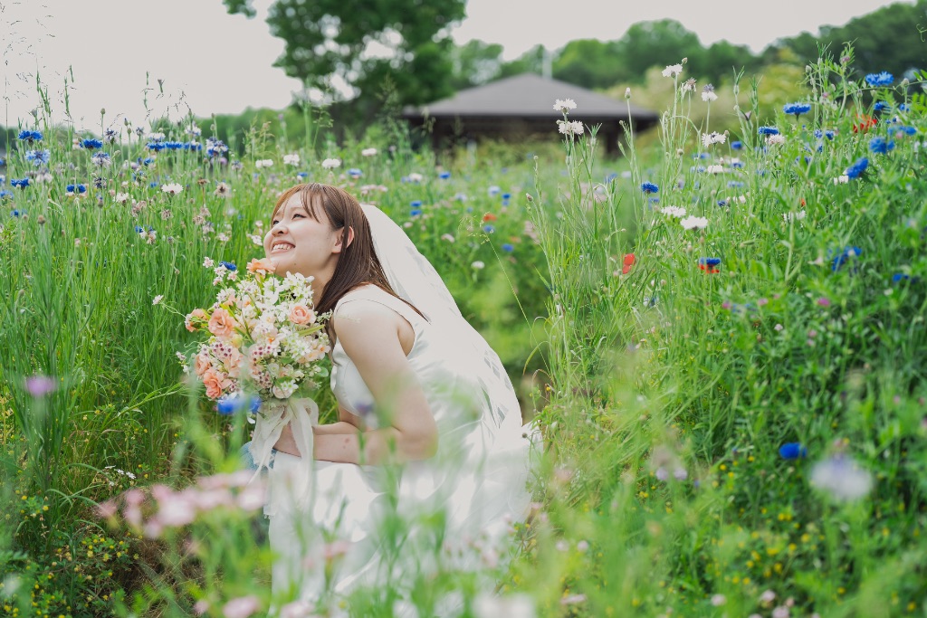 青い花畑の中に座って空を見上げる花嫁