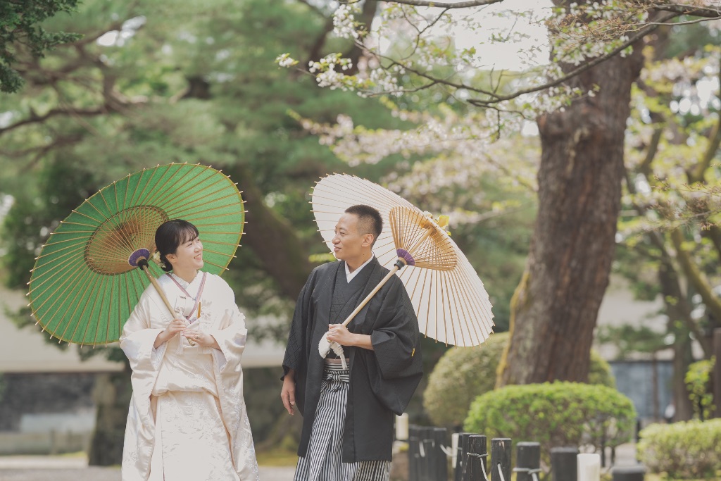 桜の下で番傘をさして歩く着物カップル