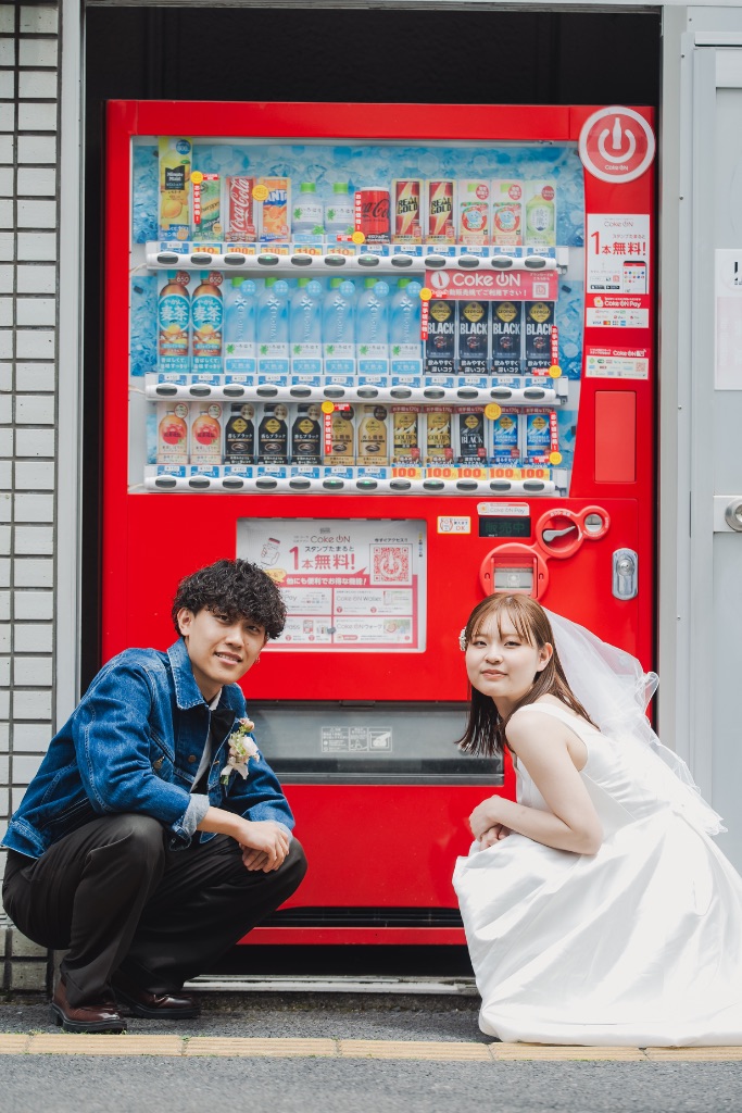 赤い自動販売機の前でしゃがむカップル